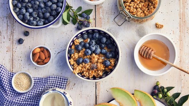 Granola with natural yogurt, fresh blueberries, nuts and honey, delicious breakfast or dessert, top view. Healthy eating concept. Stop motion animation.