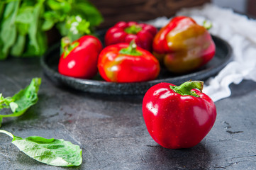 Close up red sweet bell pepper with water drops and metal tray with a few more pepper, basil on the dark textured background. Selective focus. Space for text