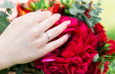 Obraz na płótnie Canvas Close up of incognito woman holding beautiful hand with golden wedding ring on colorful bouquet. Jewelry with diamonds. Will you merry me. Present for wife in special day, or birth day. Red flowers. 