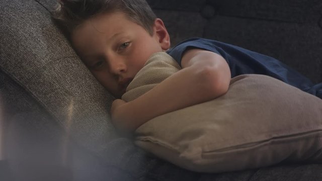Boy laying sad on the couch holding a pillow in front of him