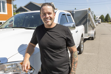 Portrait of a smiling construction worker in hardhat standing next to truck on construction site © Louis-Paul Photo
