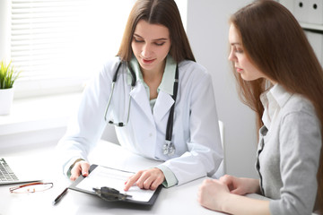 Female doctor having a talk with her patient  while sitting at the table near the window in hospital. Physician is ready to help patient. Medicine and health care concept