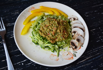 Tasty vegan meal spaghetti with zucchini, mushrooms, paprika sauce and nuts, spinach, basil and spices. Healthy green food on big plate on black wooden background.