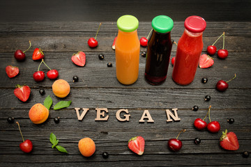Three bottles with juice, fruit and inscription vegan on a dark wooden background, food concept