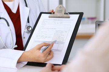 Fototapeta premium Close up of a female doctor pointing into an application form while consulting patient