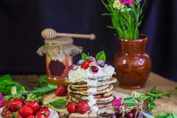Obraz na płótnie Canvas Delicious pancakes with berries on the authentic wooden stand. Summer food still life concept. Pancakes sprinkled with powder and cream