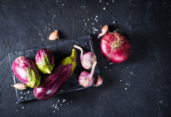Some eggplants, garlic and red onion on a black board and background © Denira