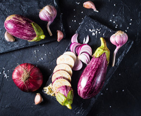 Some eggplants, garlic and red onion on a black board and background © Denira