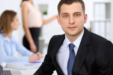 Portrait of a young business man  against a group of business people at a meeting.