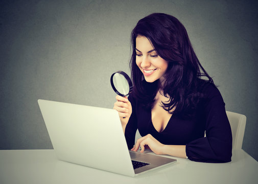 Happy Business Woman With Magnifying Glass Looking At Laptop Computer Sitting At Desk