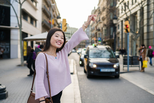 Young chinese woman asking for a cab in barcelona, raising her arm
