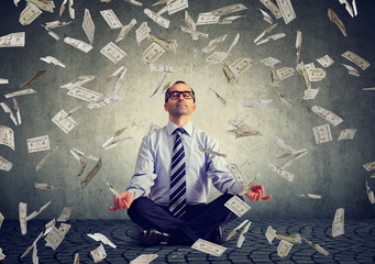 Mature business man meditating under money rain