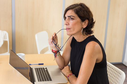 Mujer sentada frente al ordenador reflexionando con la mirada en el infinito.