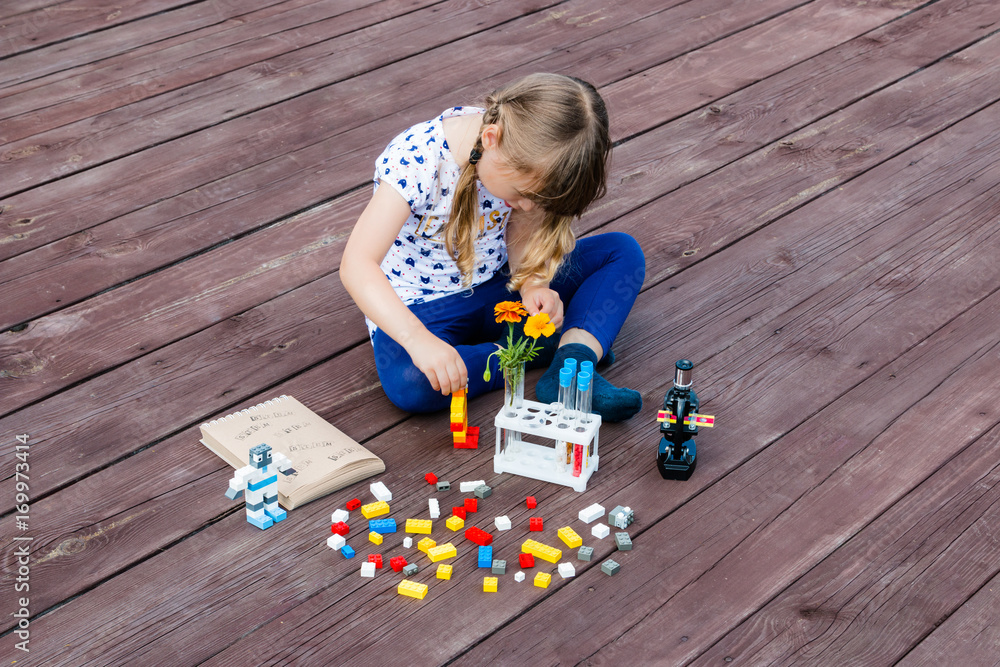 Wall mural Little girl plays on the flore. Microscope and flowers are near her. Little robots. E-learning. Stem education. Back to school.