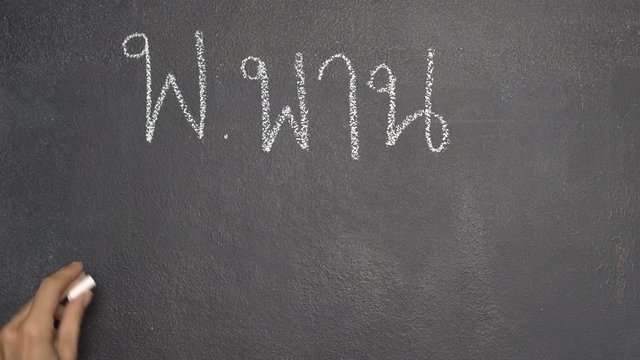 Woman's hand writing Thai letter "พ" with white chalk on blackboard