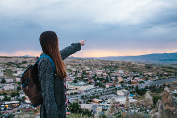 Young woman tourist with high point showing hand at sunset over the city of Goreme in Turkey....