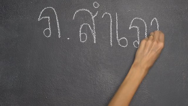 Woman's hand writing Thai letter "ภ" with white chalk on blackboard