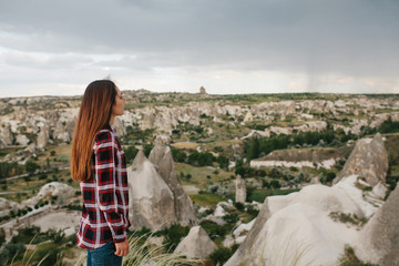 A young woman stands on a high point and looks at the view of the hills of Cappadocia in rainy...