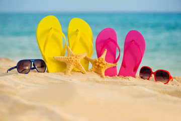 Fototapeta na wymiar Glasses with yellow and pink sandals stand in the sand against the background of the sea