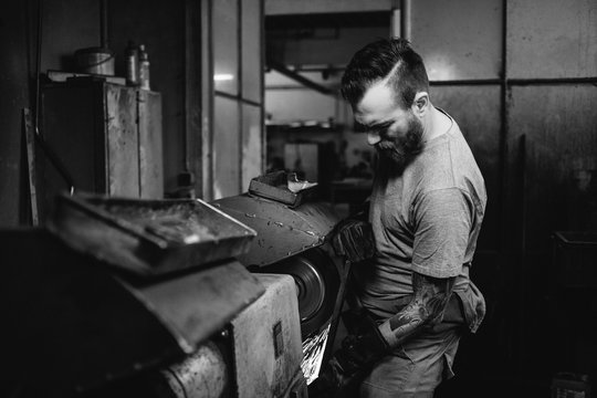 tattoed metal worker grinding metal plate in a workshop - black and white