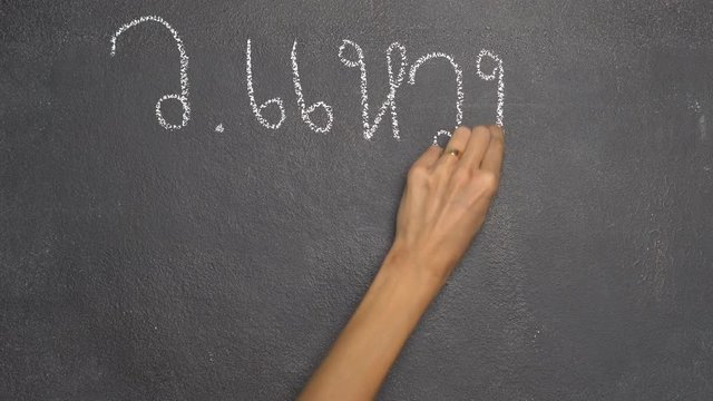 Woman's hand writing Thai letter "ว" with white chalk on blackboard