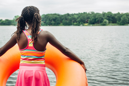 Black girl holding an orange tube by a lake
