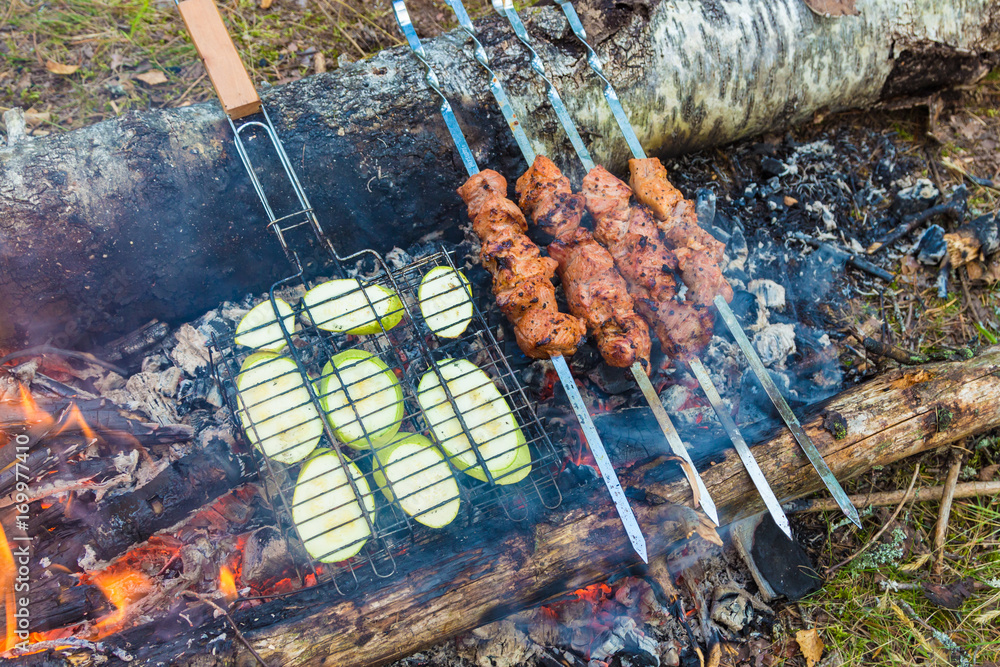 Wall mural Close up pork meat grilled on skewers. Cooking shashlik in the forest. Grilling pork on coal