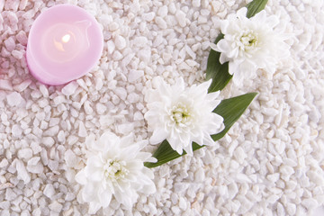 Spa. Still life. Candle, bottles with cream of pink color, a towel and flowers on a background of white pebbles. Top view