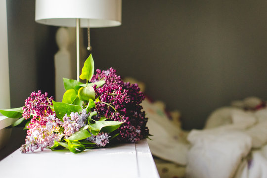Freshly cut lilacs beside an unmade bed