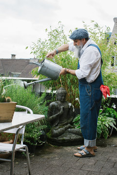 Outdoor Portrait of Cool Elderly Male Hipster Watering Plants on Balcony