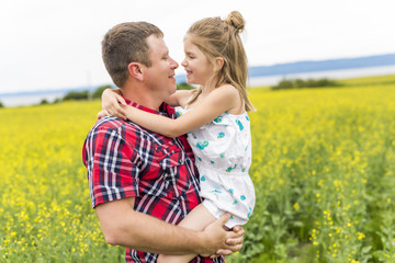 Happy family father and child daughter on yellow flowers on nature in summer