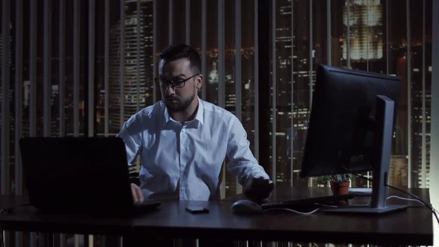 Man sitting and thinking while typing on computer in office at night.