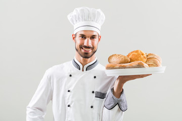 Baker holding bunch of bread on gray background.