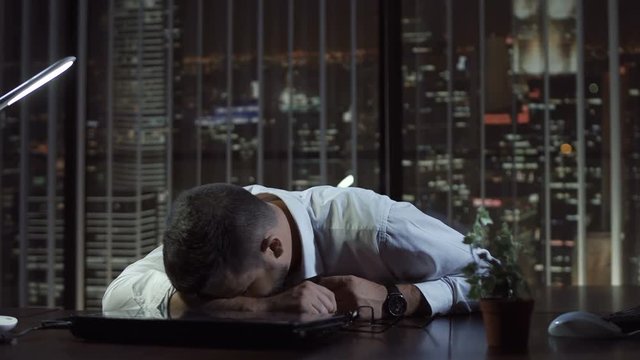Close up view of tired businessman lying and sleeping on desk in office at night.