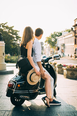 Happy young hipster couple sitting on a vintage scooter in city centre on sunset or sunrise