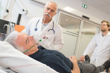 Fototapeta na wymiar patient wearing oxygen mask in hospital room visited by doctors