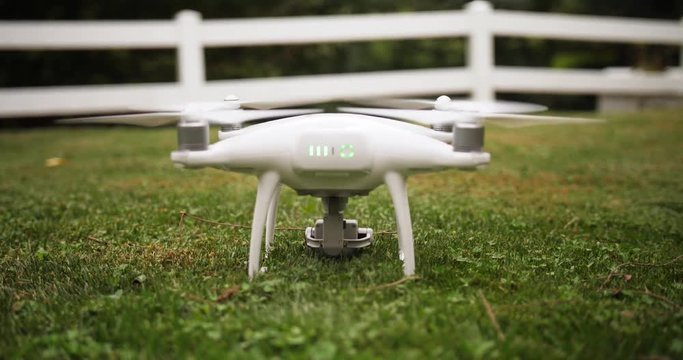 A small drone or UAV lands on a grassy field. Shot at 48fps slow motion.  	