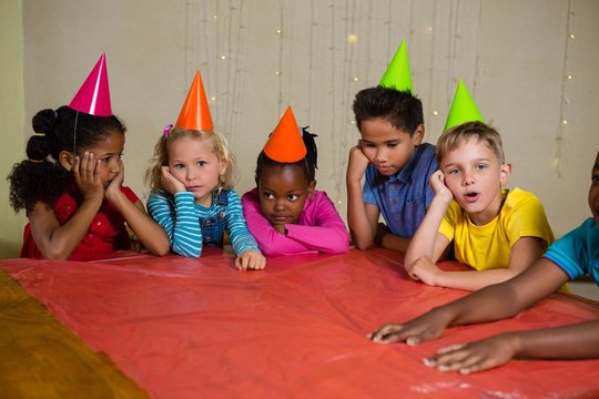 Bored children in part hat sitting at table