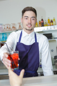 friendly young waiter serving cordial drink to client