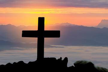 Concept conceptual cross religion symbol silhouette in nature over sunset or sunrise sky