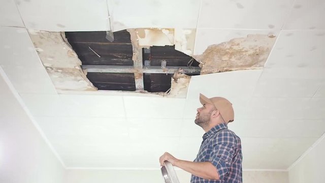 Young man call on the phone in the Service, and public utilities. Ceiling panels damaged huge hole in roof from rainwater leakage.Water damaged ceiling , Insurance case.