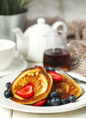 Pancakes with strawberries, blueberries and maple syrup for a breakfast.