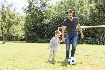 Young father with his little son playing football on football pitch