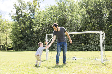 Obraz premium Young father with his little son playing football on football pitch