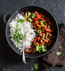 Spicy beef with vegetables and rice in a cast iron skillet on a dark background, top view. Asian...