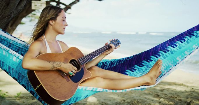 Happy young woman playing guitar on the beach