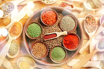 Different spices in bowls and spoons on wooden background