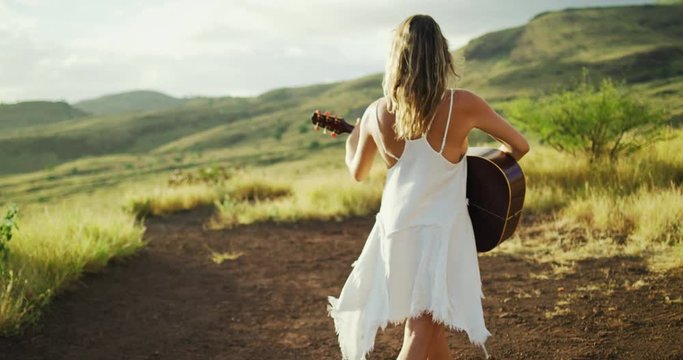 Happy young woman playing guitar at sunset
