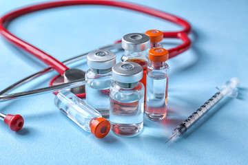 Ampules with vaccine, syringe and stethoscope on color background