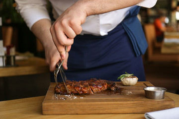 Chef cutting grilled meat on wooden board in restaurant